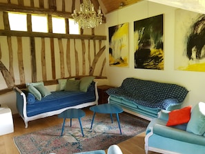 A cozy room with a blue sofa, a matching armchair, and a small table. There are abstract paintings on the wall and a chandelier hanging from the ceiling.