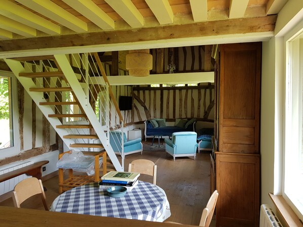 Un interior rústico con una escalera de madera, un comedor con mesa redonda y una zona de estar acogedora con sofá y sillones.