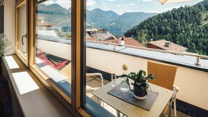 Un balcon avec une table, des chaises, un pot de fleurs et une vue sur les montagnes et les bâtiments.