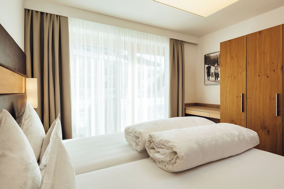 Ein Hotelzimmer mit Bett, Holzschrank, Schreibtisch und einem Fenster mit Vorhängen.