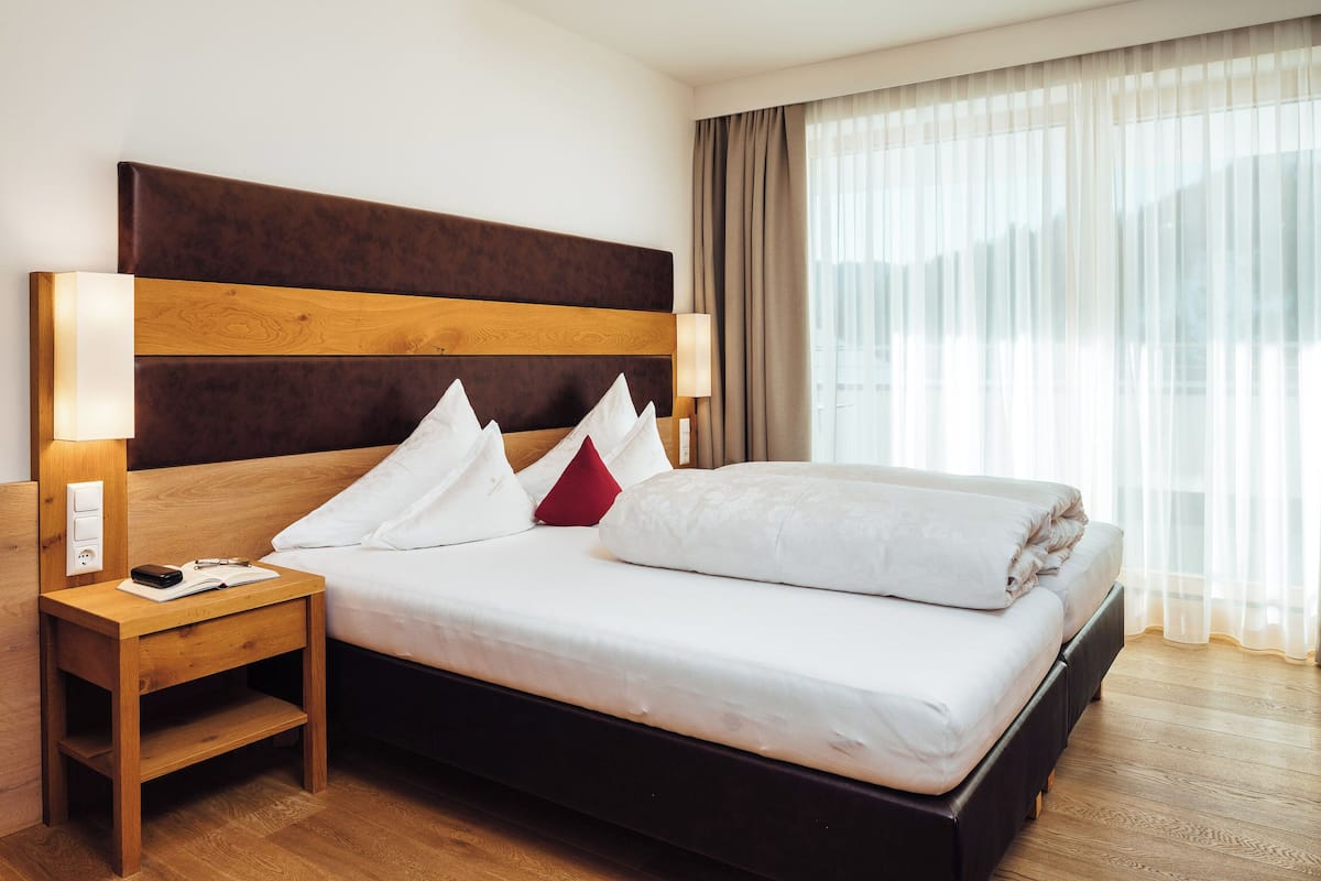 Ein Hotelzimmer mit einem großen Bett, einem Holzkopfteil, Nachttischen und einem Fenster mit Vorhängen.