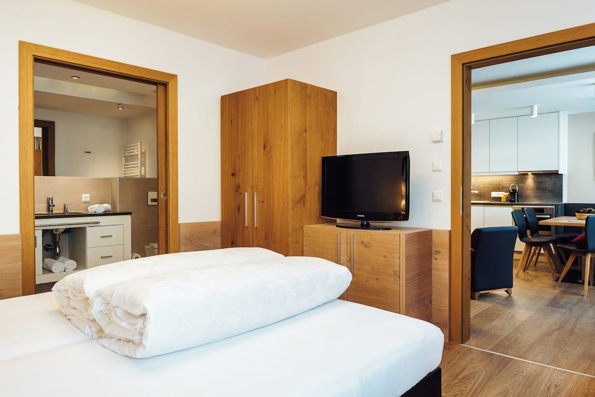 Ein modernes Hotelzimmer mit einem Bett, einem Holzschrank, einem Fernseher und einer Küchenzeile im Hintergrund.