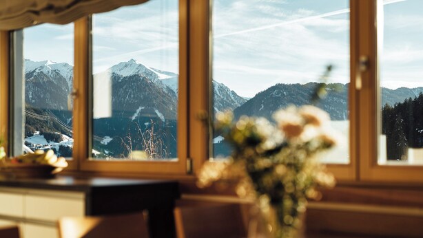 Un espace repas offrant une vue sur les montagnes enneigées grâce à de grandes fenêtres.
