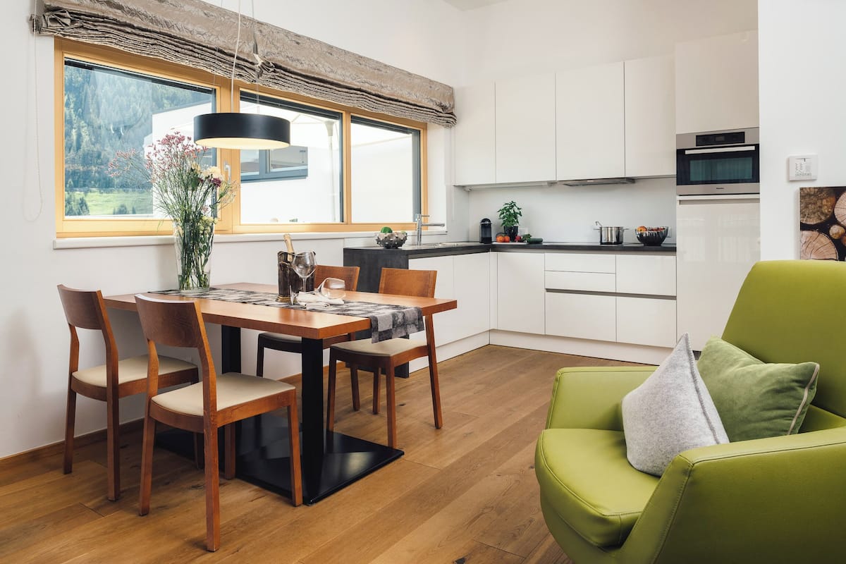 Eine moderne Küche mit weißen Schränken, einem Esstisch mit Stühlen und einem grünen Sofa.