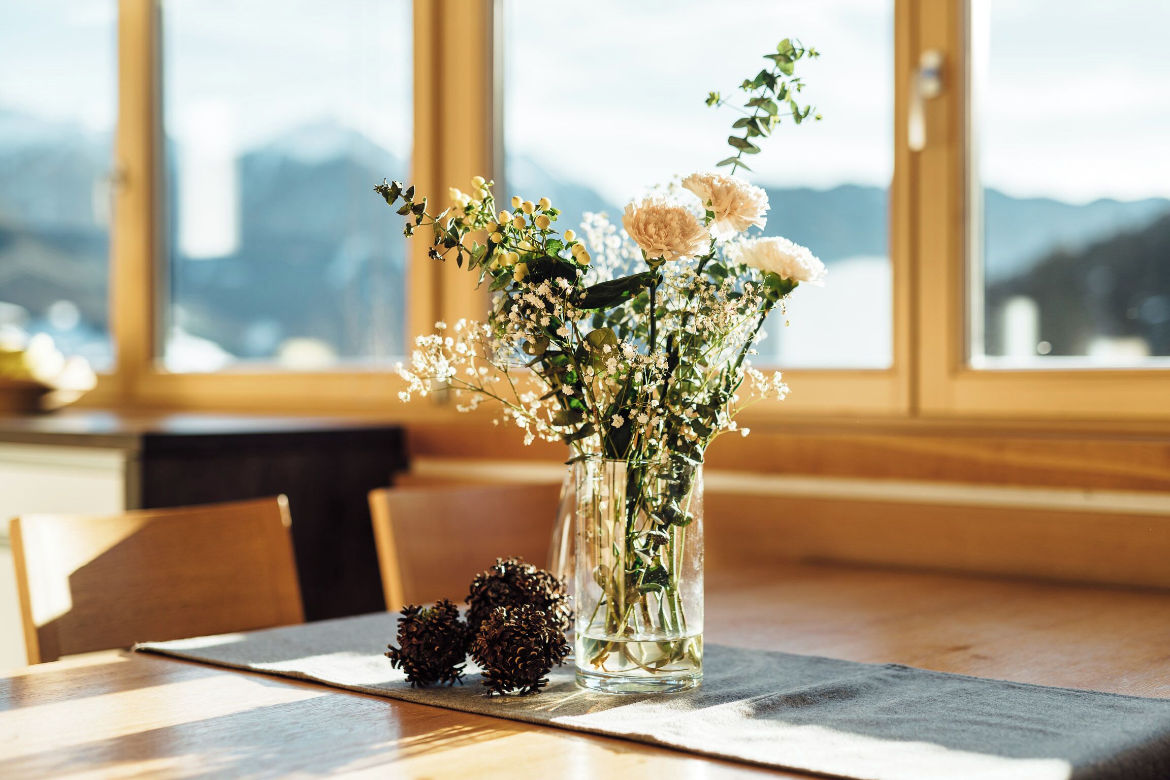 A table with a vase of flowers and pine cones on a placemat.