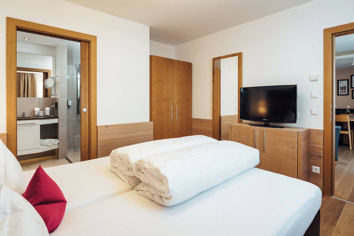 Ein Hotelzimmer mit Bett, Fernseher, Holzschrank und angrenzendem Badezimmer.