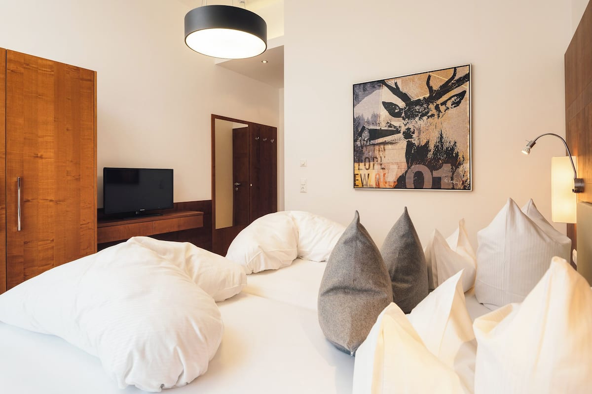 Ein Hotelzimmer mit einem Bett, Kissen, einem Fernseher, einem Holzschrank und einem Wandbild.