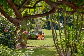 Une statue d’un enfant dans un jardin, entouré d’une végétation luxuriante et de diverses plantes.
