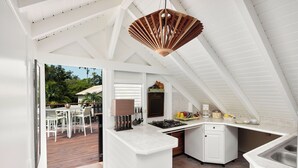 A modern kitchen with white cabinetry, a wooden ceiling fan, and a view of an outdoor patio with a dining table and chairs. - Domaine de Néron - Ti-Punch (Le Moule)