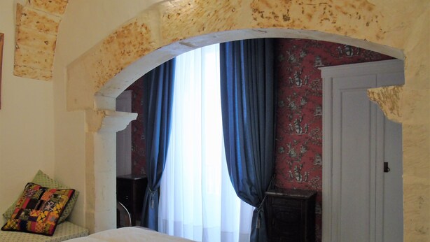 A bedroom with a large bed, a small table, a chair, and a door. -   XIXth century VILLA BASSO in Gargano- holiday rental overlooking the sea (Mont Sant'Angelo)