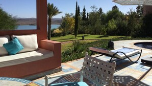 Un espacio de estar techado al aire libre con vistas a un lago y montañas.
