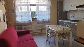 A compact kitchen with a dining table and chairs, a red sofa, and a window with sheer curtains. - Romantic two-room apartment overlooking the Sienese countryside (Sant'Andrea A Montecchio)