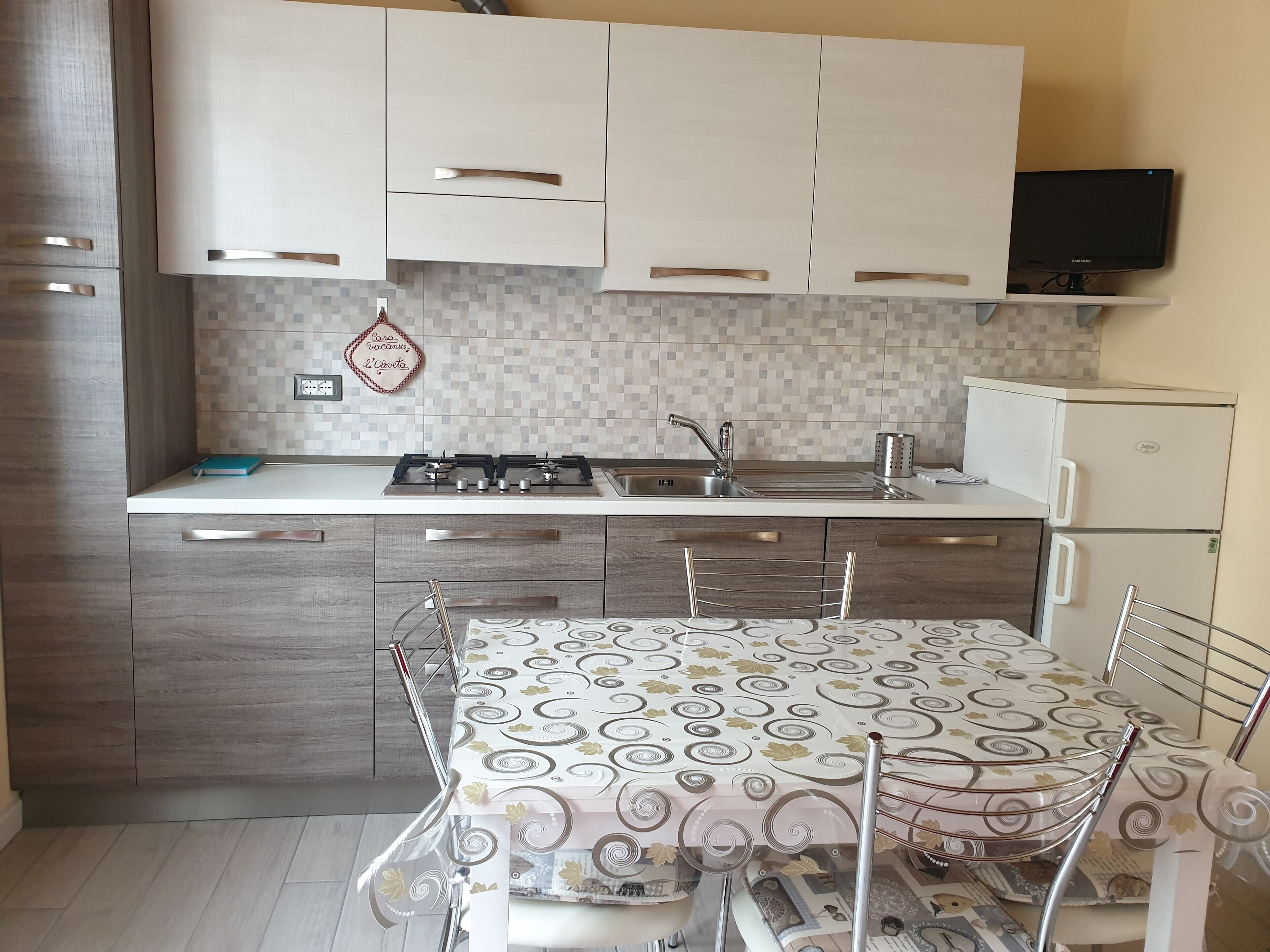 A modern kitchen with white cabinets, a gas stove, a sink, and a refrigerator.