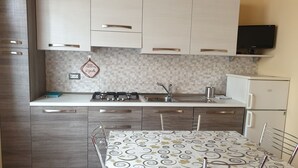 A modern kitchen with white cabinets, a gas stove, a sink, and a refrigerator. - Romantic two-room apartment overlooking the Sienese countryside (Sant'Andrea A Montecchio)