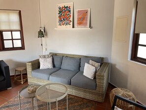 A living room with a grey sofa, wicker furniture, a small round table, and two wall-mounted artworks. - Aruba Villa with Pool, just 3 minutes driving from Aruba's best beaches (Noord)