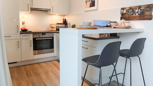 Une cuisine moderne avec des armoires blanches, un four encastré, un petit îlot central avec des tabourets de bar et un luminaire suspendu.