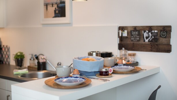 Une cuisine moderne avec un plan de travail blanc, un luminaire suspendu noir et une planche en bois sur laquelle sont disposés des aliments.