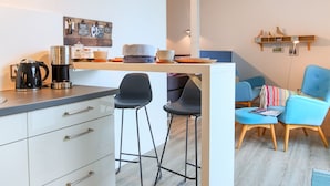 Une cuisine moderne avec des meubles blancs, une machine à café et un coin repas comprenant des chaises bleues et une petite table.