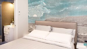 A bedroom with a bed, a nightstand, a wall mural, and a bathroom with a sink and towel rack.