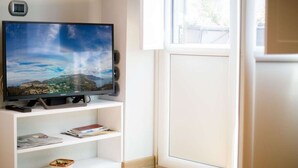 A room with a flat-screen TV on a white stand, a window with a view of a mountain, and a door.