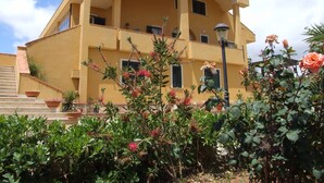 Ein mehrstöckiges Gebäude mit Balkonen, einer Treppe und einem Garten mit Blumen.