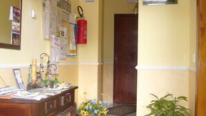 A hallway with a wooden desk, a fire extinguisher, a bulletin board, and a potted plant. - B & B St. ELIA suite ROSA: CHARMING VILLA IMMERSED IN THE HISTORIC PARK DUBINI (caltanissetta)