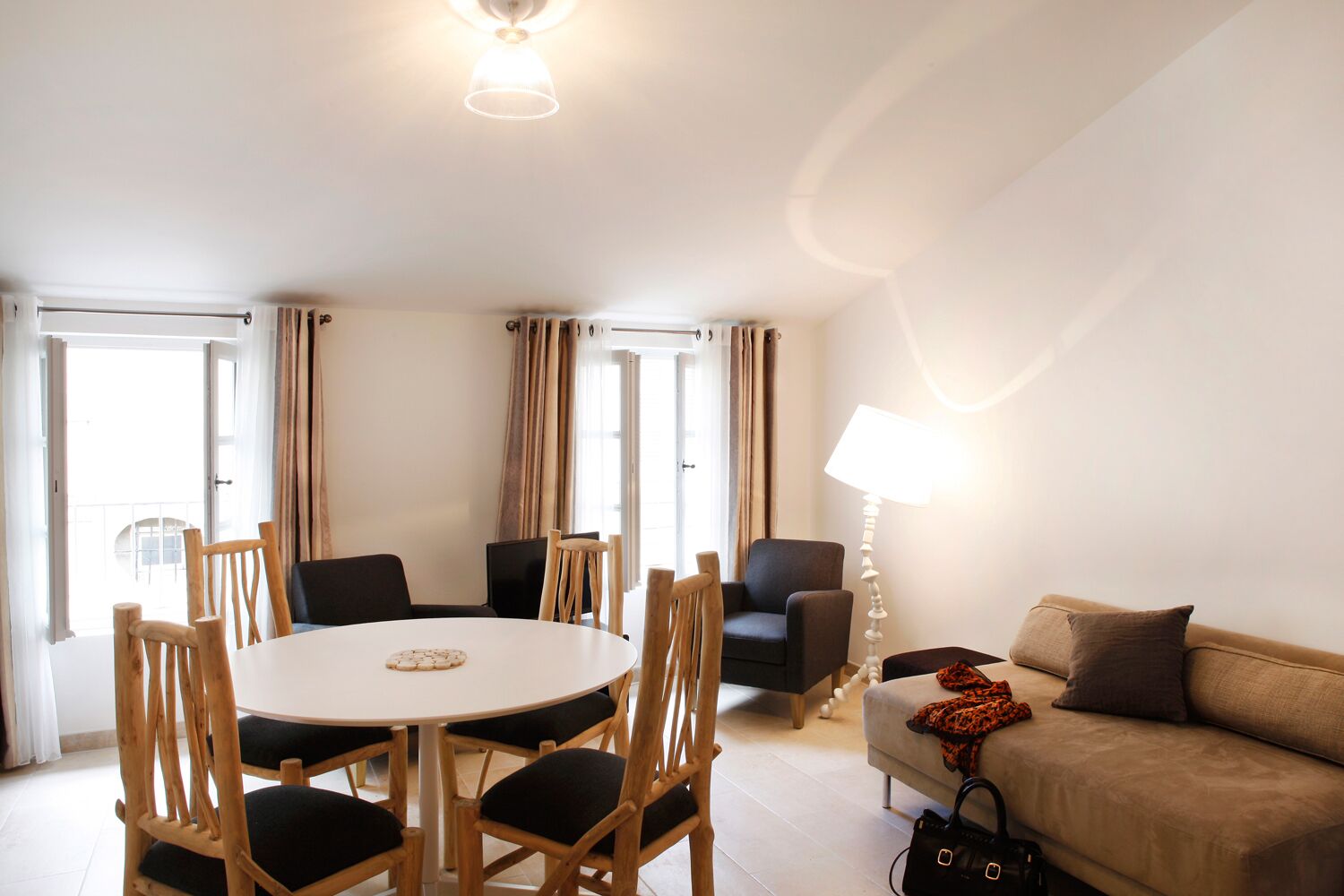A modern living room with a round dining table, wooden chairs, a sofa, and a lamp.