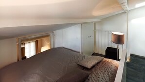 Een kleine, goed verlichte slaapkamer met een enkel bed, een nachtkastje, een lamp en een garderobe.