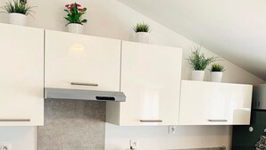 Een moderne keuken met witte kasten, een roestvrijstalen fornuis en een inbouwoven. Op het aanrecht staan potplanten en er is een klein spoelgedeelte.