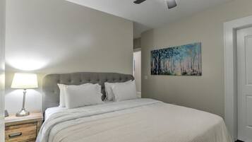 A bedroom with a bed, a nightstand, a lamp, a ceiling fan, and a painting on the wall.