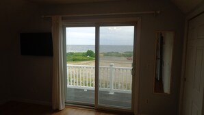 Een kamer met een grote schuifglazen deur die leidt naar een balkon met uitzicht op de oceaan.