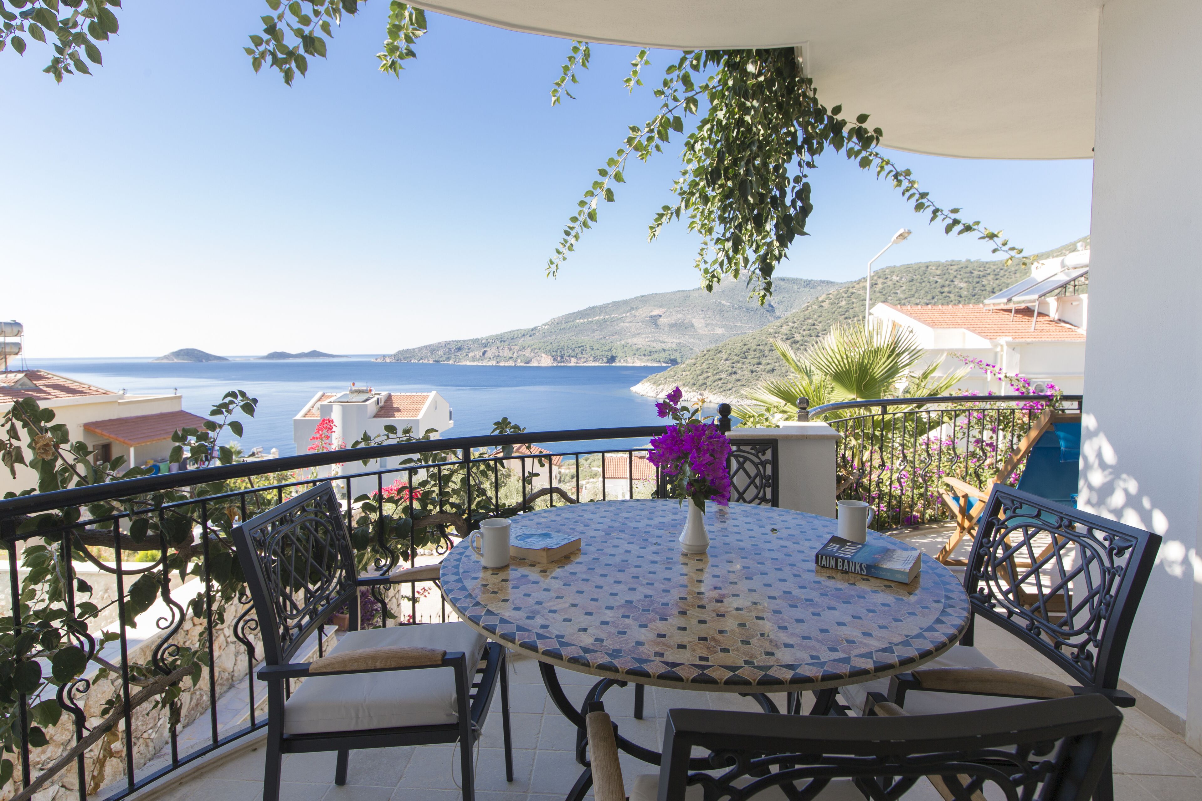 Uma varanda com vista para o mar, uma mesa redonda com cadeiras e um vaso de planta.