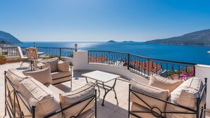 Eine Terrasse mit Gartenmöbeln, Meerblick und einer Berglandschaft.