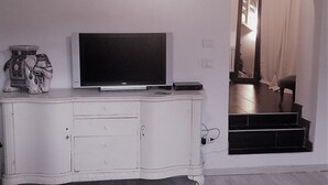 A room with a white cabinet, a flat-screen TV, and a mirror reflecting a staircase.