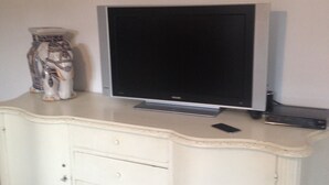 A white cabinet with a flat-screen TV on top, a remote control, and a decorative vase.