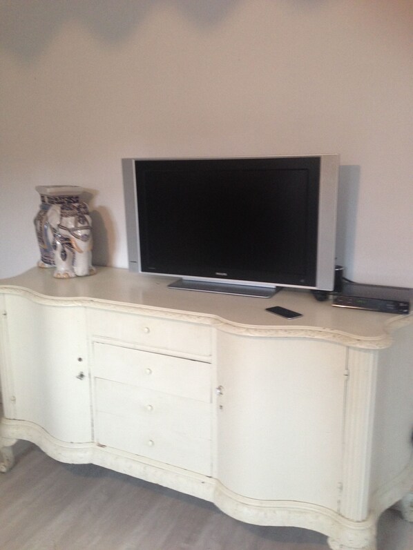 Ein weißes Sideboard mit einem Flachbildfernseher darauf, einer Fernbedienung und einer dekorativen Vase.