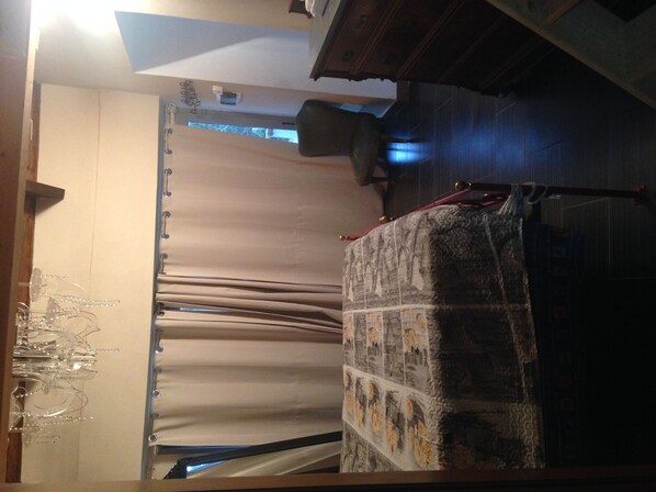 A room with a bed covered by a patterned blanket, a window with curtains, and a chair.
