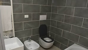 A small bathroom with a bidet, toilet, and bathtub.