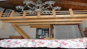 A loft-style bedroom with a wooden ceiling and a chandelier.
