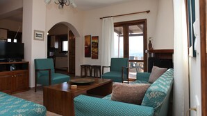 Un salon avec des canapés à motifs turquoise, une table basse en bois et un téléviseur posé sur un meuble. On y trouve deux fauteuils, une petite table et un tableau accroché au mur.
