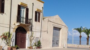 A building with a large arched entrance, a balcony, and a garage door. There are potted plants in front of the building.