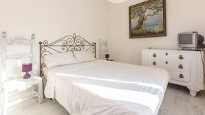 A bedroom with a bed, a dresser, a television, and a painting on the wall.