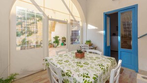 A room with a table covered in a floral tablecloth, white chairs, and a blue door.