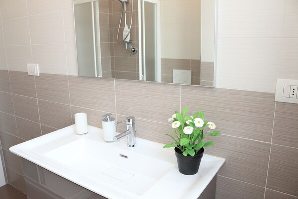 A bathroom with a white sink, a mirror, and a potted plant with white flowers.