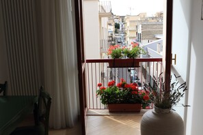 A balcony with a wooden floor, a chair, a potted plant with red flowers, and a white vase with a plant.