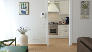 A modern kitchen with white cabinets, a stove, and a coffee maker. There is a vase with flowers on the wall and a painting of flowers. - Holiday ABOUT THEATRE (Matera)