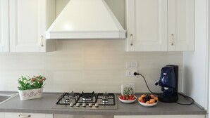 A kitchen with white cabinets, a gas stove, a coffee machine, and a bowl of fruit. - Holiday ABOUT THEATRE (Matera)