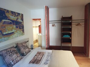 Un dormitorio con cama, armario, un cuadro y un baño visible a través de una puerta abierta.