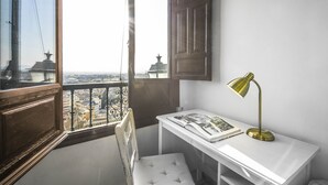 Une chambre d’angle avec vue sur la ville, un bureau blanc, une chaise et une lampe de bureau en laiton.