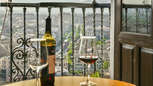 Un balcon donnant sur une vue de la ville, une bouteille de vin et un verre à vin vide.